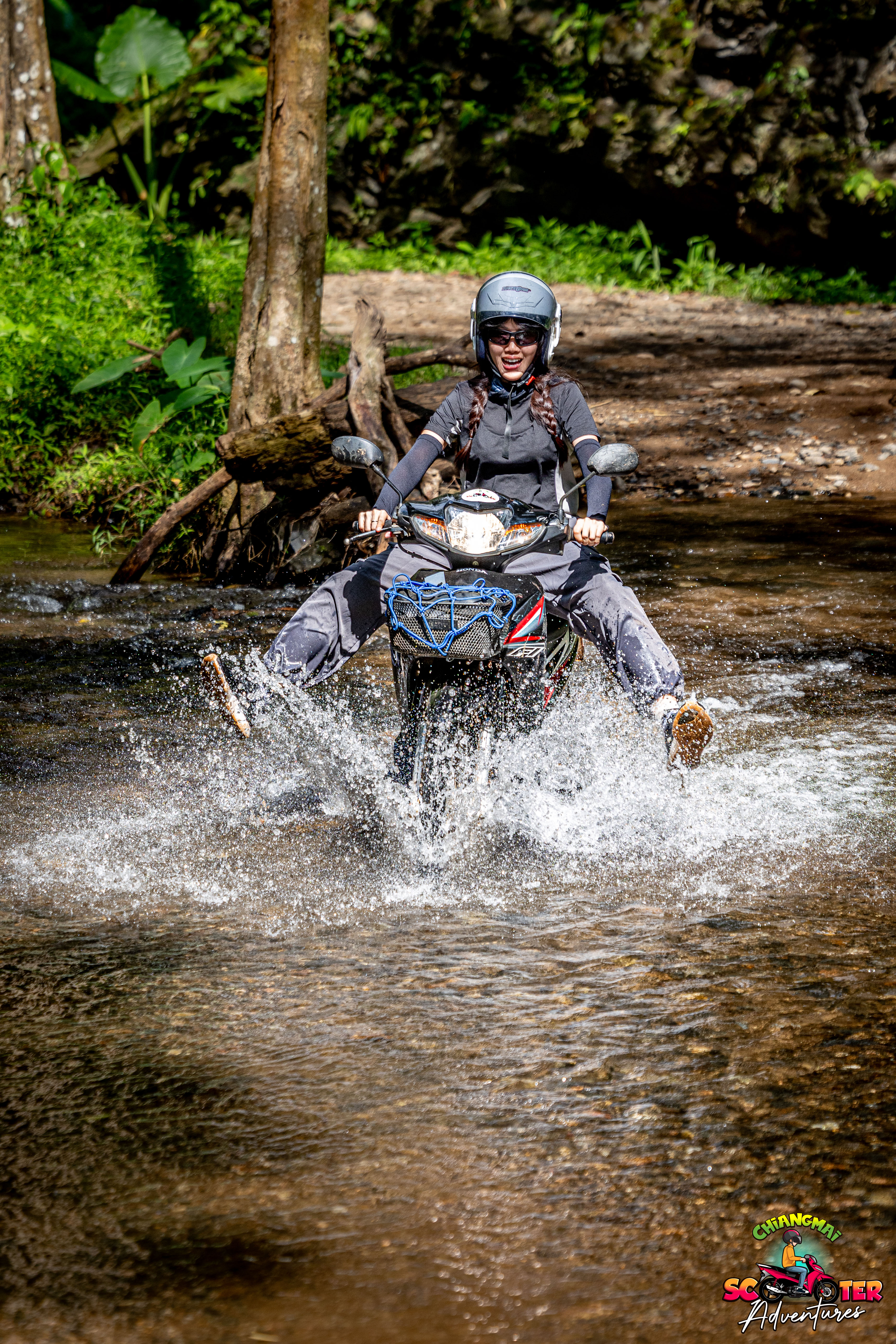 Rider on a scooter splashing through a shallow forest stream in Chiang Mai